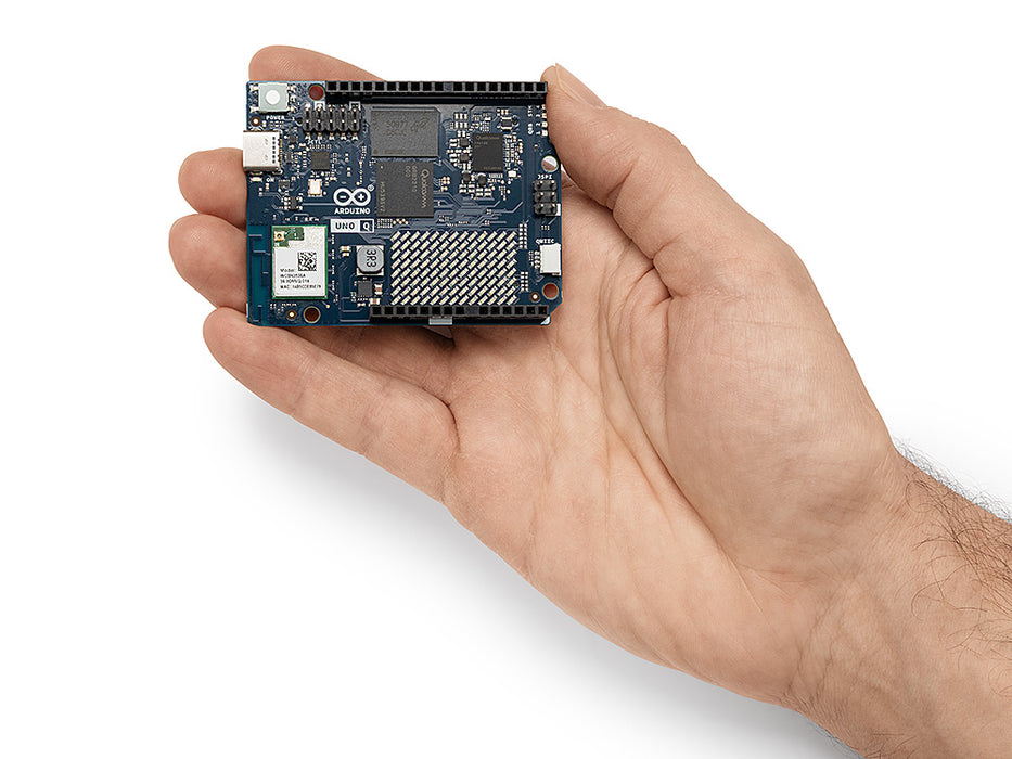 A hand holding the compact Arduino Uno Q single-board computer, demonstrating its small form factor and layout of the Qualcomm Dragonwing processor and STM32 MCU.
