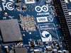 Close-up macro of the Arduino Uno Q printed circuit board (PCB) featuring the Qualcomm Dragonwing logo and surface-mount electronic components.