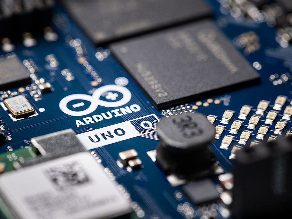 Detailed macro shot of the Arduino Uno Q circuit board, showing the official Arduino logo, surface-mount components, and the Qualcomm Dragonwing processor on the blue PCB.
