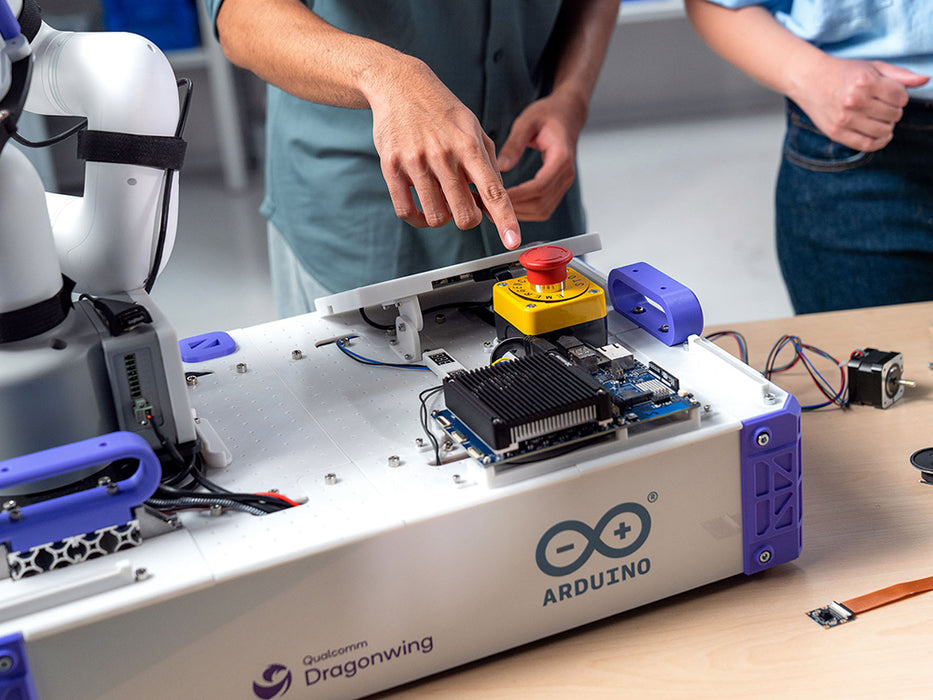Context photo of the Arduino VENTUNO Q mounted on a robotic arm workstation, showing the board's heatsink, cabling, and an emergency stop button nearby.