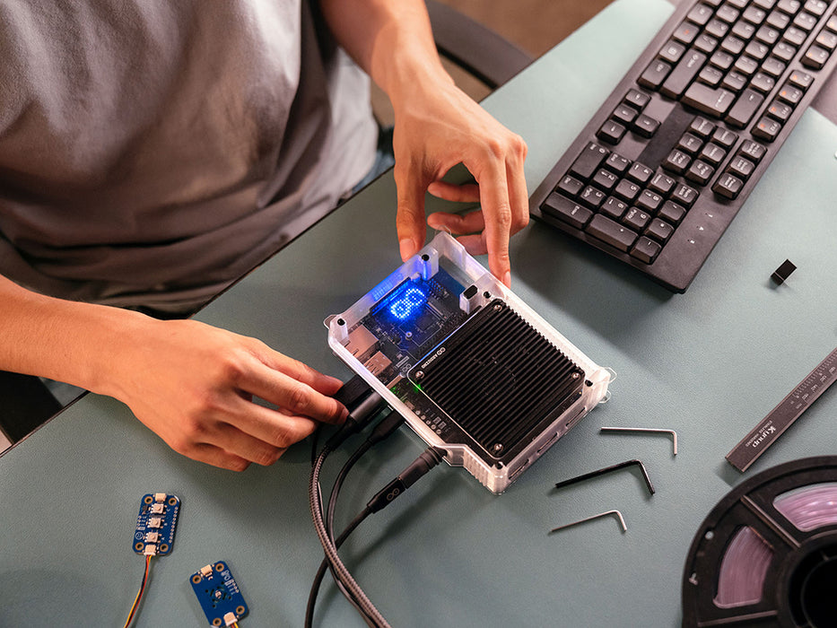 Top-down view of hands assembling the Arduino VENTUNO Q into its clear enclosure, showing the illuminated status display, heatsink, and camera sensor boards.