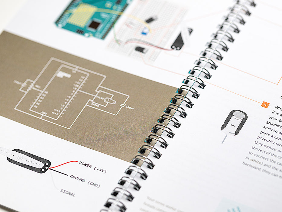 Macro shot of the Arduino project book, open to detailed technical illustrations. Shows a circuit diagram with a 100pF capacitor and a component pinout for Power, Ground, and Signal.