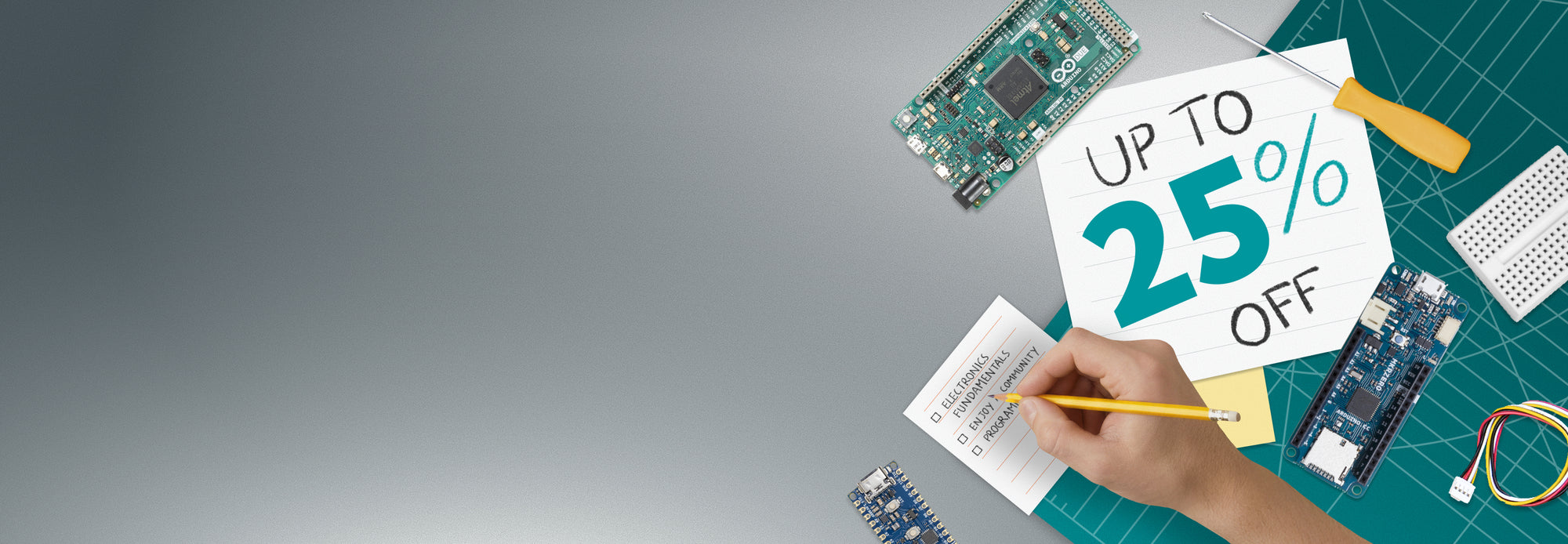 A panoramic banner for the Arduino Store winter sale featuring an overhead view of a green cutting mat workspace. On the right, various electronic components like an Arduino Due, a breadboard, and jumper wires surround pieces of paper. The largest paper displays "UP TO 25% OFF" in hand-drawn teal and black lettering. A hand is shown holding a yellow pencil, ticking off items on a checklist that includes "ELECTRONICS FUNDAMENTALS," "ENJOY COMMUNITY," and "PROGRAMMING."